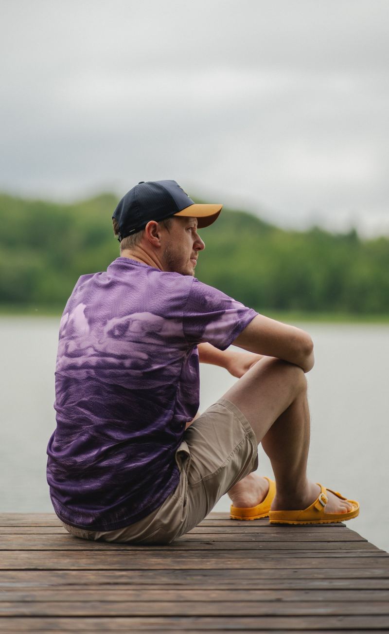 Man sitting on a lake pier in a purple patterned shirt